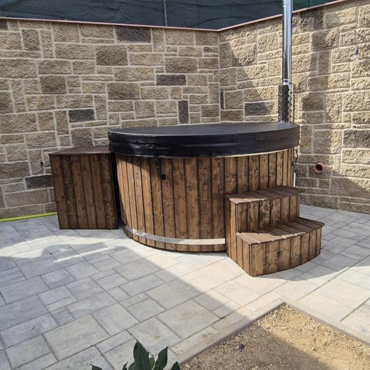 polarsauna shop Hot Tub 200 cm mit Holzverkleidung, Treppe und Ofen in einem Garten auf einer Steinterrasse