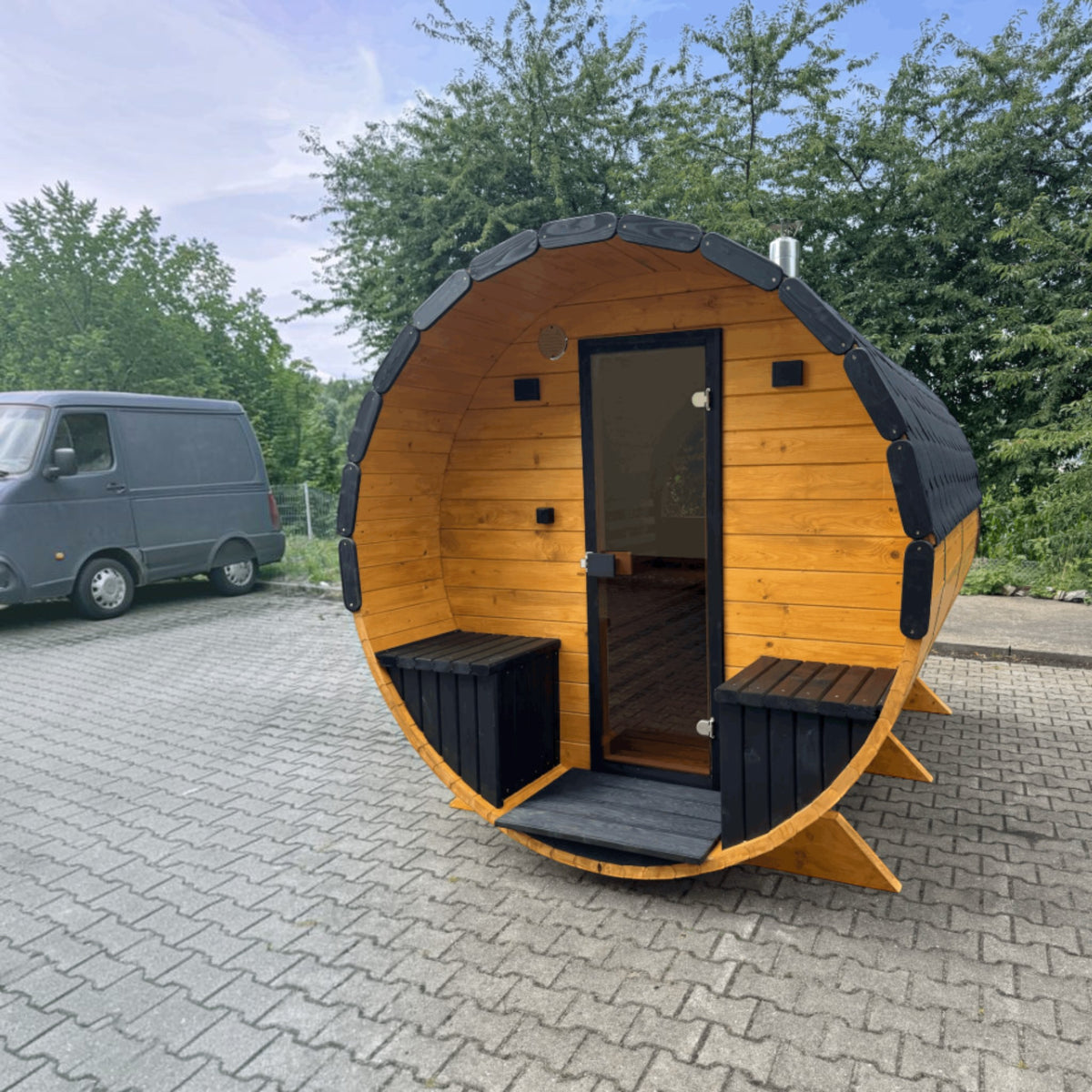 polarsauna shop Fasssauna Highline aus massiver Fichte mit schwarzer Tür und Dachschindeln im Außenbereich