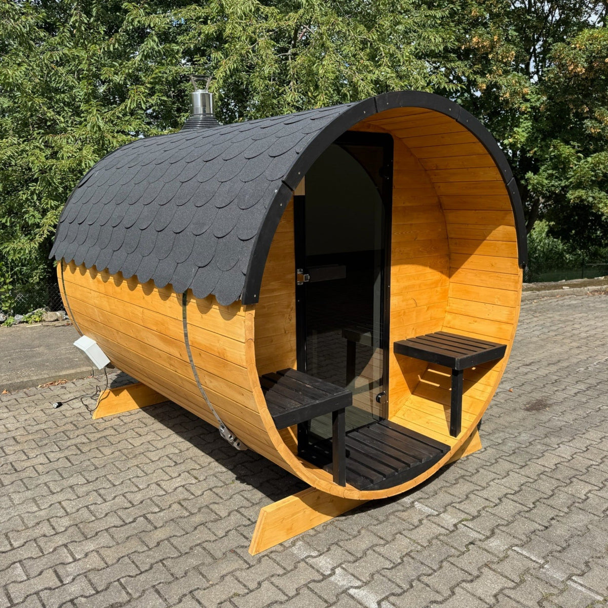 polarsauna shop Fasssauna Trendline aus Fichtenholz mit schwarzem Schindeldach und Sitzbank im Außenbereich
