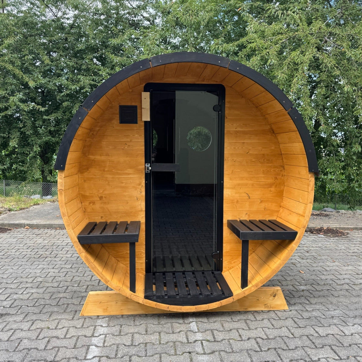 polarsauna shop Fasssauna Trendline aus Fichtenholz mit schwarzer Glastür und zwei Außensitzen im Garten