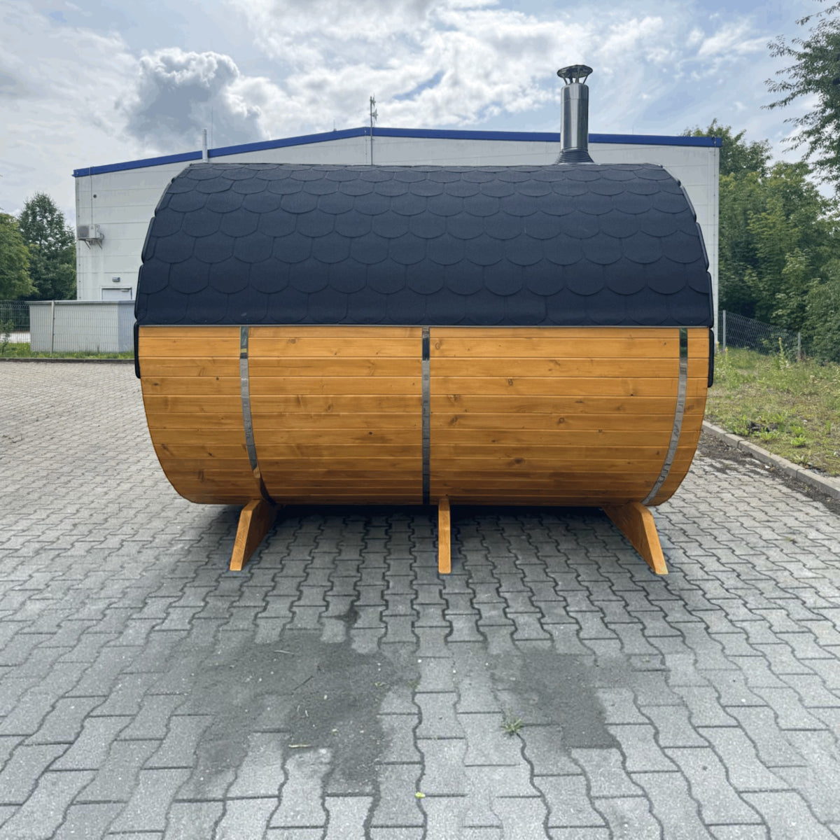 polarsauna shop Fasssauna Highline aus massiver Fichte mit schwarzem Schindeldach und Holzofen im Außenbereich
