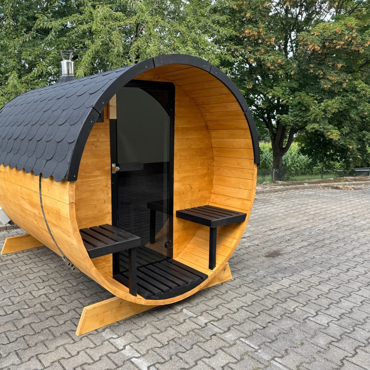 polarsauna shop Fasssauna Trendline aus Fichtenholz mit schwarzem Dach und Glaseingang im Außenbereich
