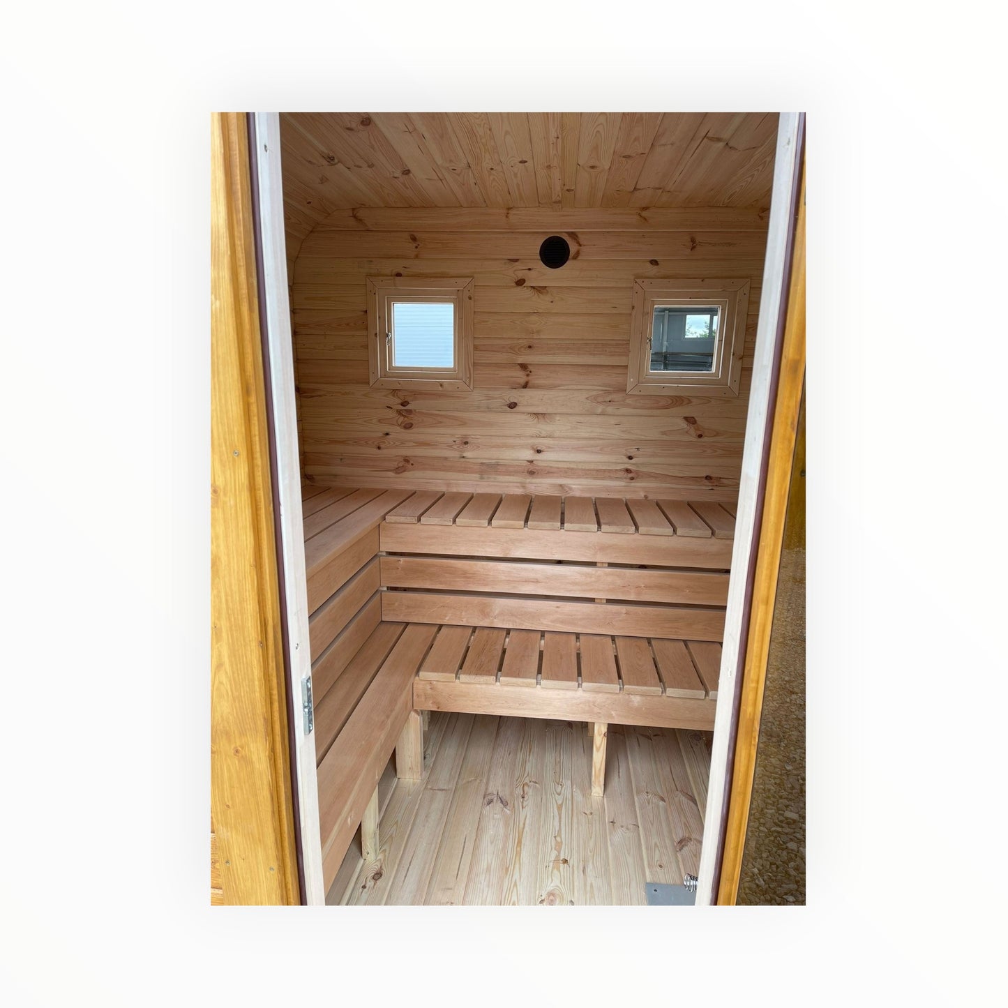 Innenansicht einer polarsauna shop Gartensauna mit hellen Holzsaunabänken und zwei kleinen quadratischen Fenstern