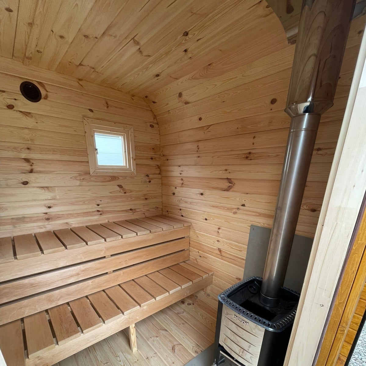 Innenansicht der polarsauna shop Quadro-Sauna 2M mit Fichtenholz-Wänden, zwei Sitzbänken und einem Harvia-Holzofen.