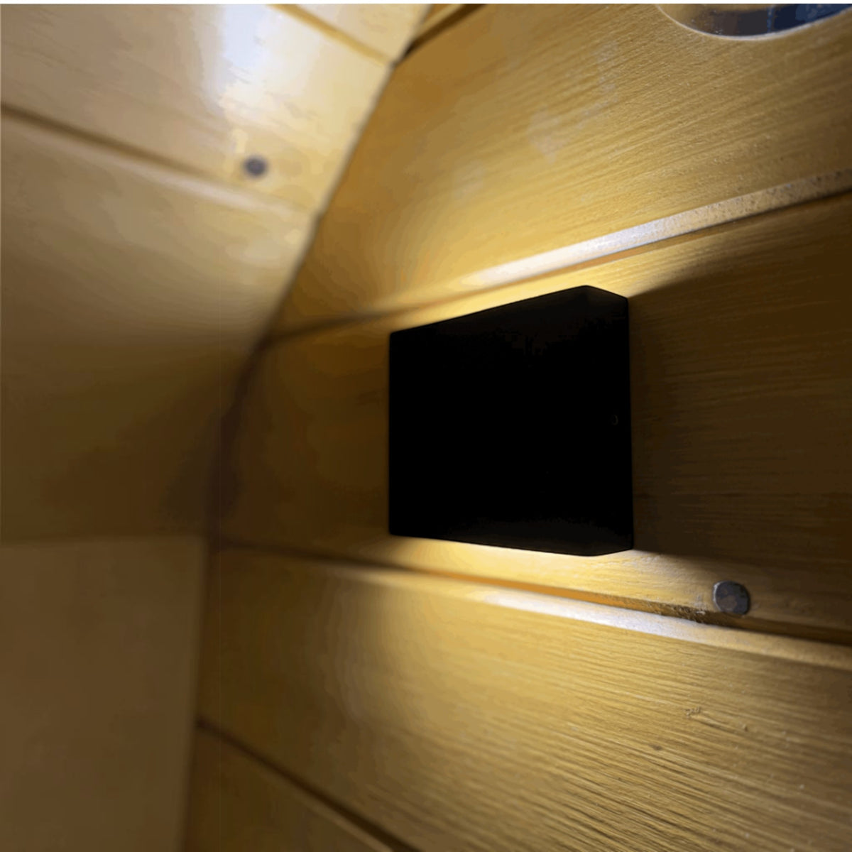 Moderne schwarze LED-Saunaleuchte an einer hellen Fichtenholzwand in einer polarsauna shop Fasssauna